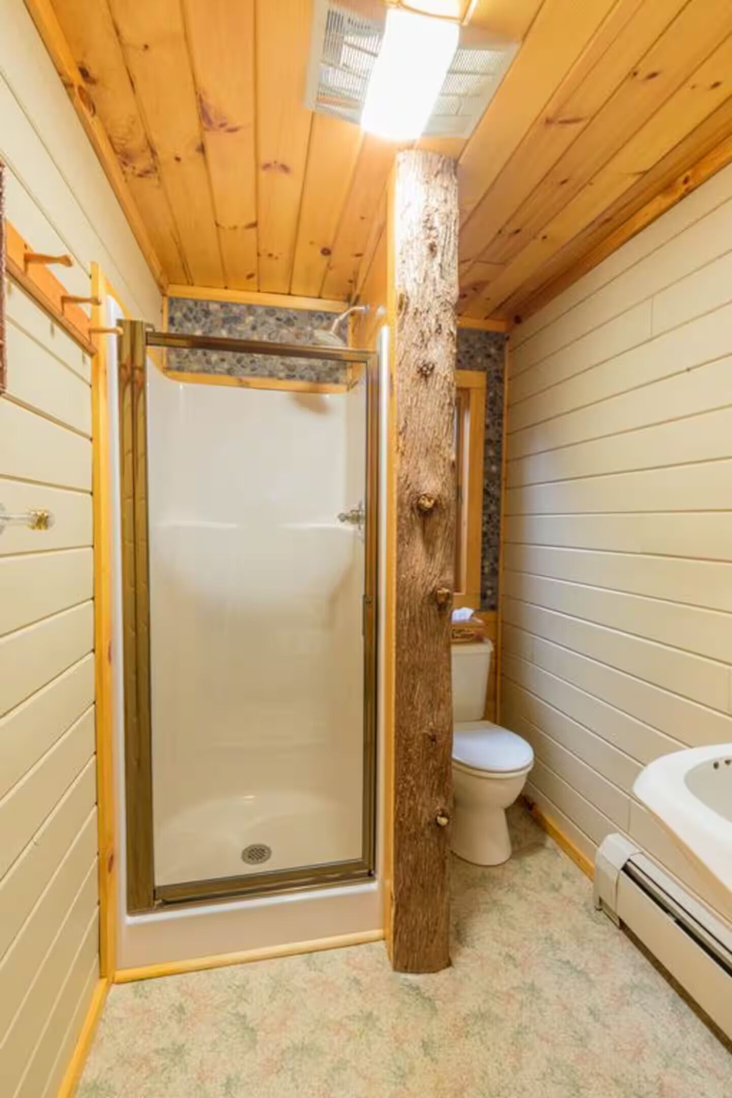 Une salle de bain aux murs lambrissés, dotée d’une douche à parois de verre, de toilettes et d’une baignoire.