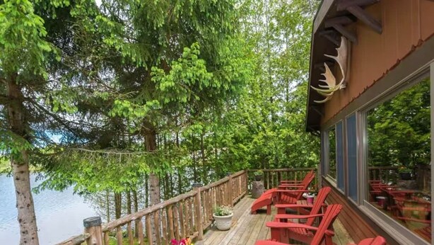 Puinen terassi, jossa on punaiset Adirondack-tyyliset tuolit, ja josta avautuu näkymä järvelle. Terassin ympärillä on puita.