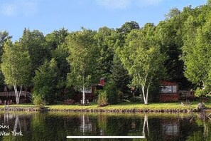 Um imóvel à beira do lago com uma casa rodeada por árvores densas e um corpo d'água calmo.