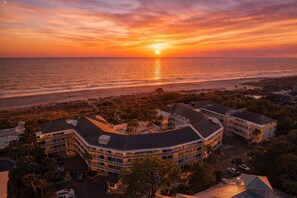 Ein Hotel an der Küste mit gebogener Architektur, Blick auf den Strand und einem Sonnenuntergang über dem Meer.