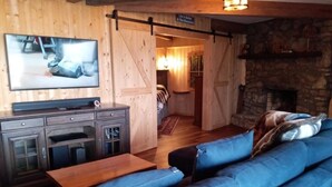 Tunnelmallinen huone, jossa on sininen sohva, puukaapit, televisio ja kivinen takka.