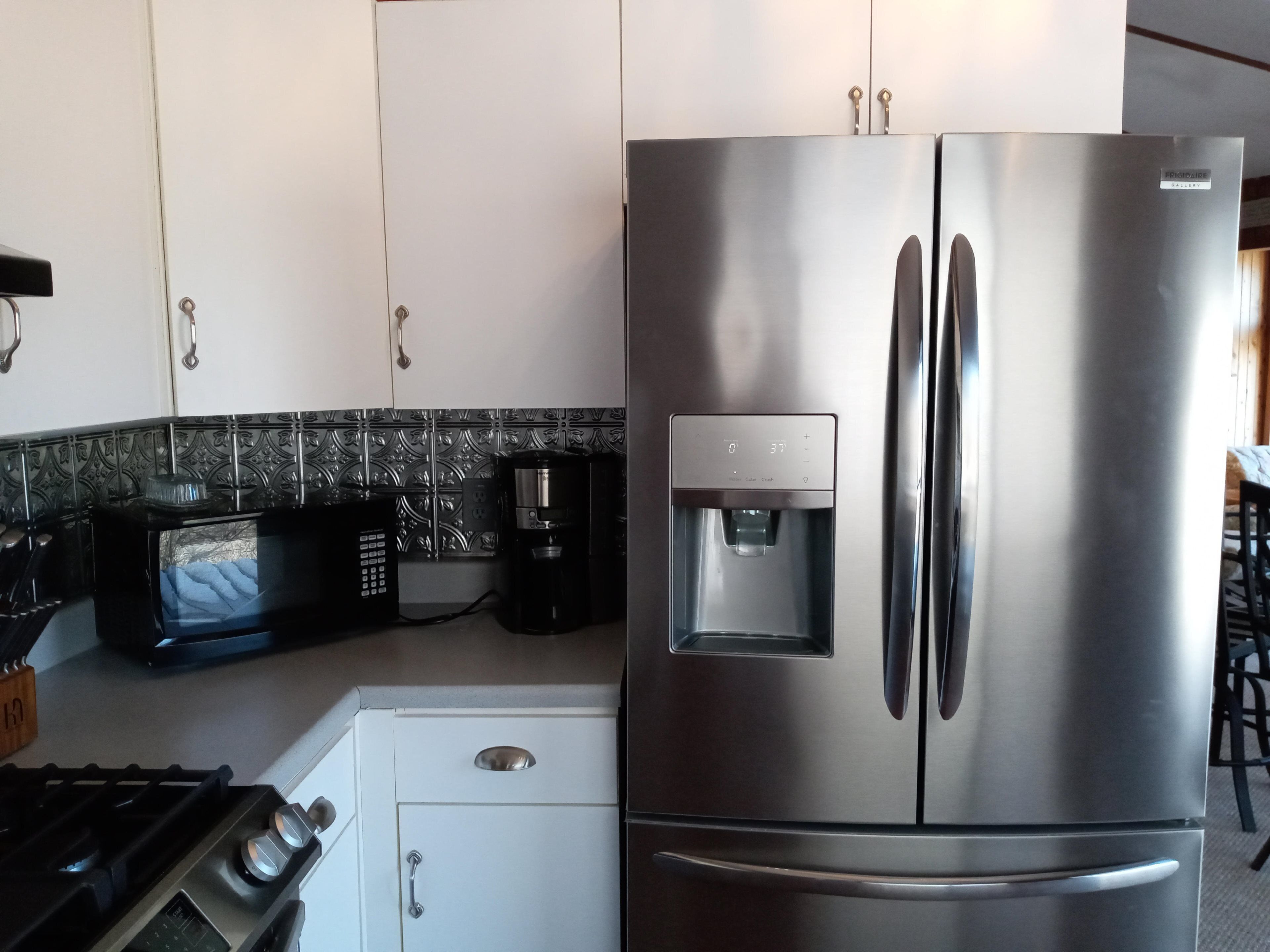 Ein Edelstahl-Kühlschrank mit Wasserspender, Mikrowelle und Kaffeemaschine auf einer Küchenarbeitsplatte.