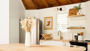 Une cuisine moderne avec un plafond en bois, des meubles blancs, un îlot central avec deux chaises et un luminaire suspendu.