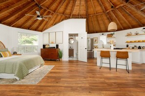 A spacious bedroom with a large bed, a wooden dresser, and a view of the kitchen.