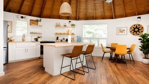 Une cuisine moderne avec des meubles blancs, un îlot central en bois et un coin repas doté de chaises jaunes.