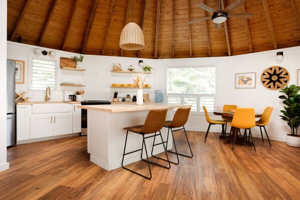 A modern kitchen with white cabinets, a wooden island, and a dining area with yellow chairs.