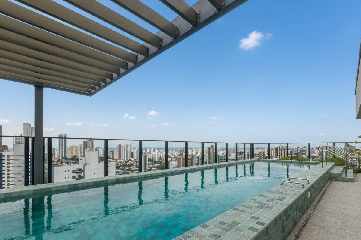 Ein Infinity-Pool auf dem Dach mit Blick auf die Stadt, einer Pergola und einem Sicherheitsgeländer.