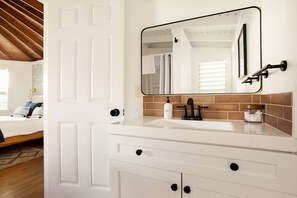 A bathroom with a white vanity, a large mirror, and a sink with a black faucet. - Ohia Cottage Volcano Hawaii (Volcano)
