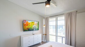 Ett modernt hotellrum med en stor säng, en platt-TV som är monterad på väggen, ett sängbord och ett fönster med gardiner.