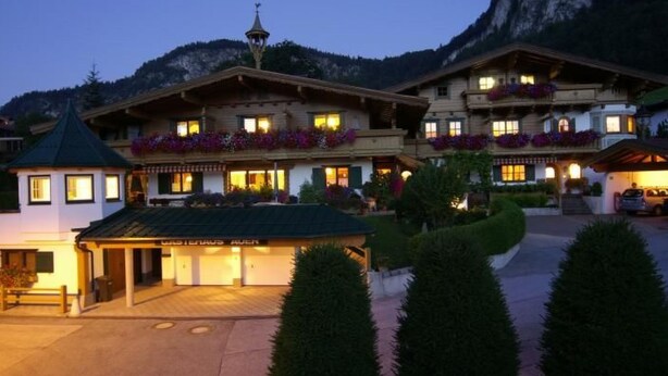 A hotel with a traditional Alpine architectural style, featuring multiple balconies with flower boxes, a well-lit entrance, and a view of the surrounding mountainous landscape. - in ruhiger Lage nahe am See by Interhome (Thiersee)