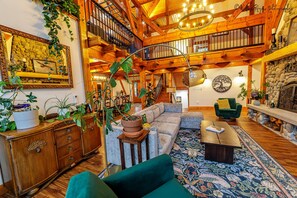 Amplia sala de estar con techo alto, vigas de madera, una escalera y una chimenea acogedora.