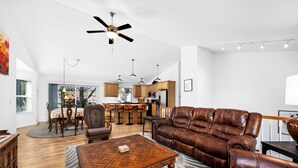Un salon spacieux avec un canapé en cuir marron, une table basse en bois et un ventilateur de plafond.