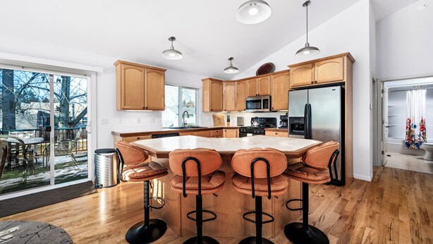 Une cuisine moderne avec des meubles en bois, un grand îlot central doté de tabourets, des appareils en acier inoxydable et un éclairage suspendu.