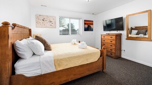 Une chambre à coucher avec un lit en bois, du linge de lit blanc, une commode, un téléviseur et des œuvres d’art accrochées aux murs.