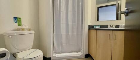 A bathroom with a toilet, shower curtain, and wooden cabinets.