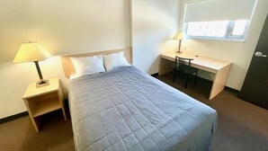 Une chambre d’hôtel avec un lit, un bureau, une chaise et une fenêtre avec des stores.