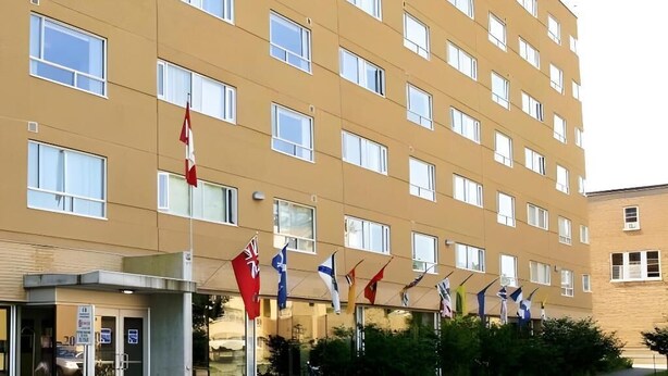 A multi-story hotel with a beige facade, numerous windows, and a row of flags at the entrance. - Résidence Saint-Paul - Quiet, practical living in Ottawa (Ottawa)