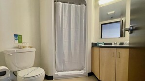 A bathroom with a toilet, shower curtain, and wooden cabinets. - Résidence Saint-Paul - Quiet, practical living in Ottawa (Ottawa)