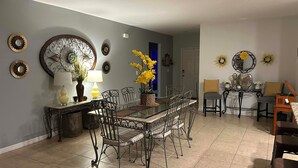 Een eethoek met een glazen tafel, metalen stoelen en decoratieve wandkunst.