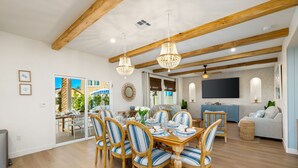A dining area with wooden tables and chairs, a chandelier, and a view of the outdoors. - Isle of Palms: Sleeps 27, Lazy River & Waterslide (Indio)