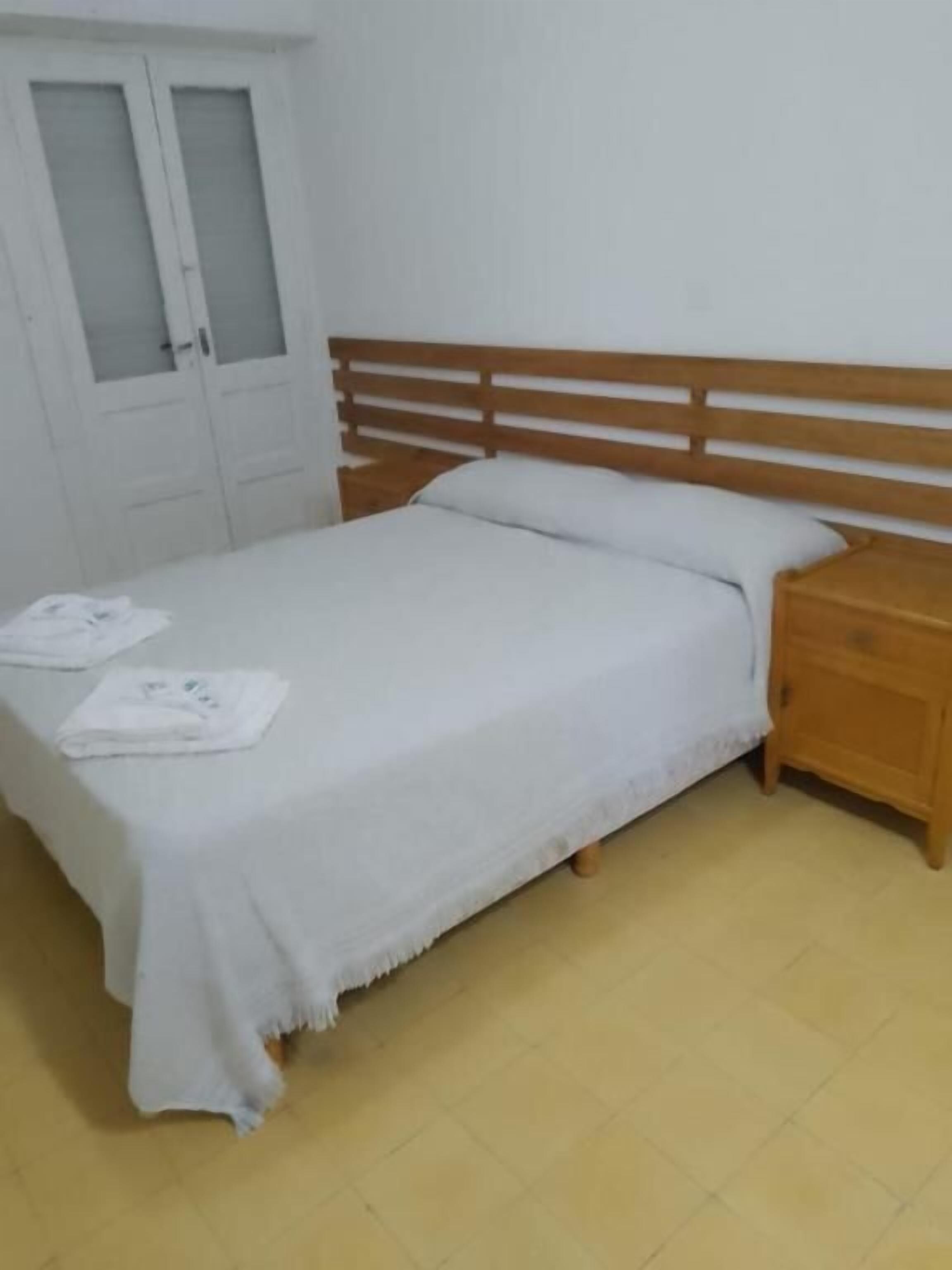 A single-bed room with a wooden headboard, a wooden nightstand, and a white bedspread.