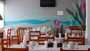A restaurant with tables set for dining, a TV mounted on the wall, and a colorful mural on the wall. - Hotel Costamar Miramar (Miramar)