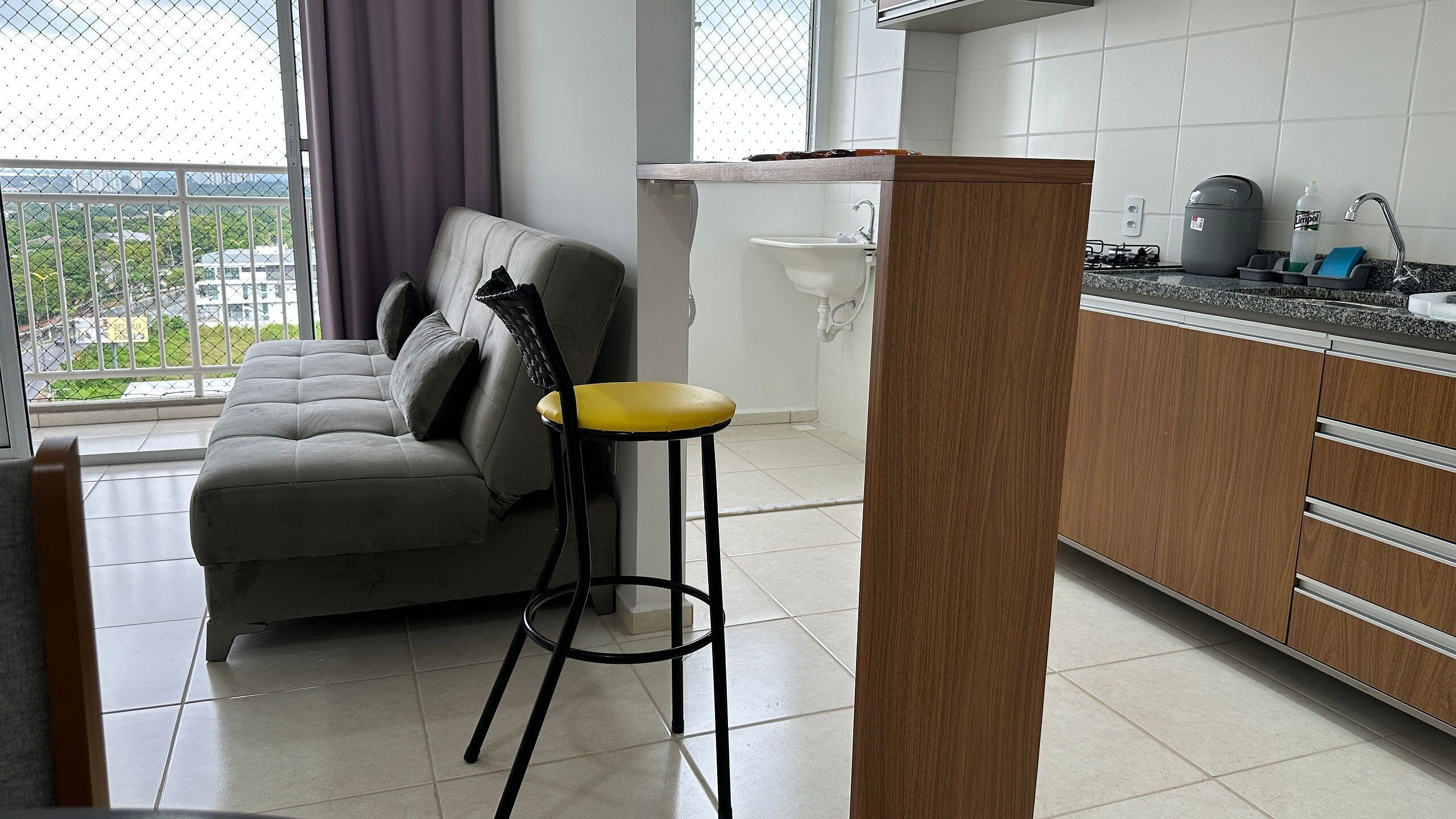 Une cuisine moderne avec un canapé gris, un tabouret en bois et une vue par la fenêtre.