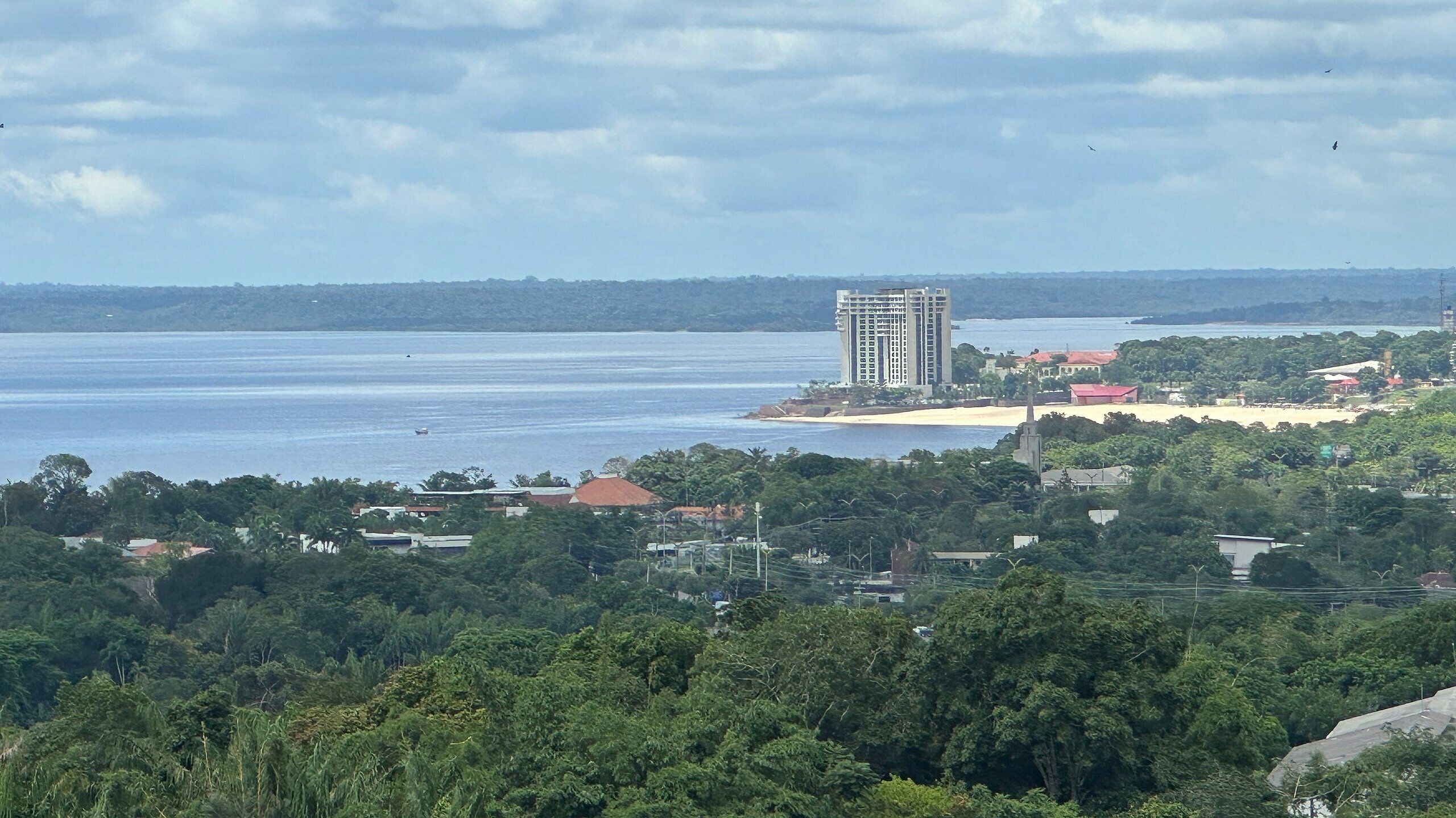 Vista costera con un edificio alto, una playa y abundante vegetación.