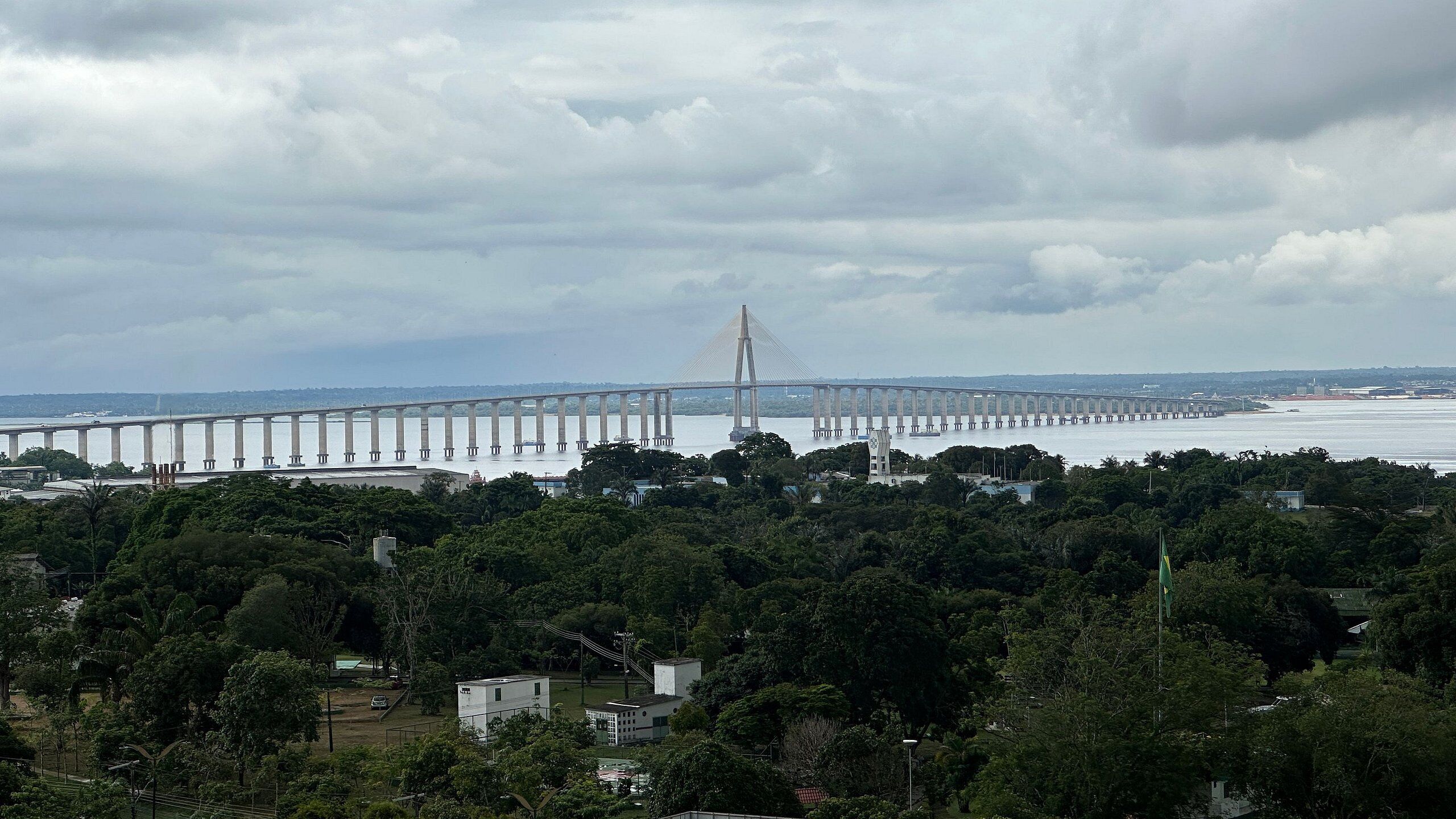 A large bridge spanning a body of water, surrounded by dense greenery and a few buildings.
