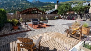Um deck de madeira com área de estar ao ar livre, um caminho de pedra e vista para uma cordilheira.