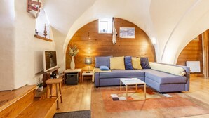 Uma sala de estar aconchegante no estilo loft, com teto de madeira, um sofá, uma TV e uma mesa pequena.