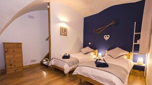 Quarto com duas camas, cómoda de madeira e teto abobadado singular.