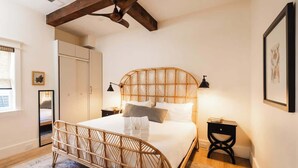 Ein Schlafzimmer mit einem Rattanbett, einem Holzbalken an der Decke, einem Nachttisch und einem Beistelltisch.