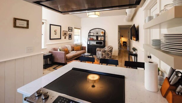 Eine moderne Küche mit Kochinsel, ein Essbereich mit Sofa und Sesseln sowie ein Wohnzimmer mit Fernseher und gerahmten Bildern.