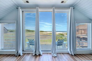 A room with large windows, a balcony with chairs, and a view of the outdoors. - Luxury 6BR Beach Retreat | Pool, Views & Priv Dock (Hilton Head Island)