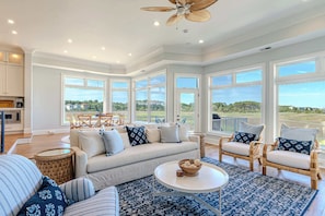 A spacious living room with a large window, a ceiling fan, and a dining area with a view. - Luxury 6BR Beach Retreat | Pool, Views & Priv Dock (Hilton Head Island)
