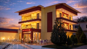 Un hotel de varios pisos con fachada roja y amarilla, entrada visible y zona de estar al aire libre.