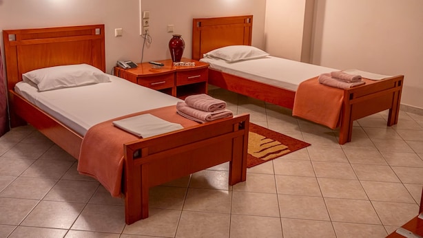 Habitación de hotel con dos camas de madera, una mesita de noche, una lámpara y una pequeña mesa.