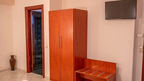 Una habitación con armario, banca, televisor y puerta que da a una zona con baldosas.