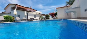 Una piscina amb gandules i ombrelles, envoltada d'edificis amb teulada de rajola i parets blanques.