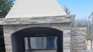 Ein aus Stein gemauerter Pizzaofen für den Außenbereich mit Schornstein, Gasflasche und Bedienfeld mit der Aufschrift 'CAMPINGAZ'.