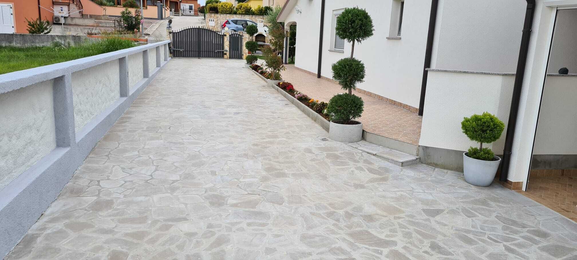 A stone-paved pathway leading to a gated entrance with potted plants and a white building.