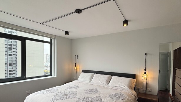 Un dormitorio moderno con una cama grande, suelo de madera, un ventanal y vistas a edificios.