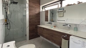 Un baño moderno con cabina de ducha de vidrio, inodoro, lavamanos con espejo y lavadora.
