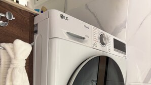 Lavadora LG ThinQ de carga frontal en un baño con un armario de madera y un perchero.