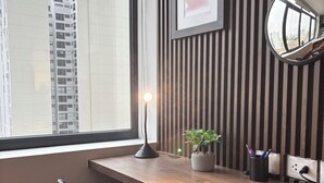 Un escritorio moderno con vistas a un paisaje urbano a través de un amplio ventanal, una planta en maceta y una lámpara de escritorio.