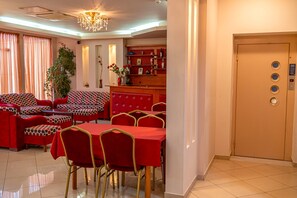 A hotel room with a dining area featuring red furniture, a chandelier, and a minibar. - Jayne s Rooms - Elassona Single Nest (Elassona)
