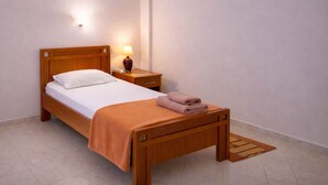 A single bed with a wooden headboard, a bedside table with a lamp, and a folded towel on the footboard. - Jayne s Rooms - Elassona Single Nest (Elassona)