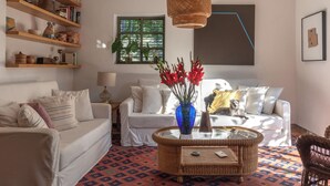 Un salon comprenant un canapé, deux fauteuils, une table basse et des étagères remplies de livres et d’objets décoratifs.