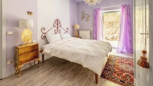 A bedroom with a bed, a chandelier, a nightstand, a lamp, and a window with curtains. - Juniper Apartment - Relax, Nature and Panorama with Private Pool (Toscana)
